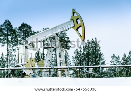 Pump jack and wellhead in the oilfield situated in the beautiful winter forest. Environmental pollution. Oil and gas concept.