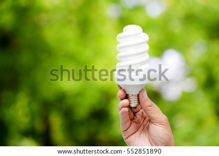 Mão segurando a lâmpada sobre fundo natural verde, conceito de energia verde