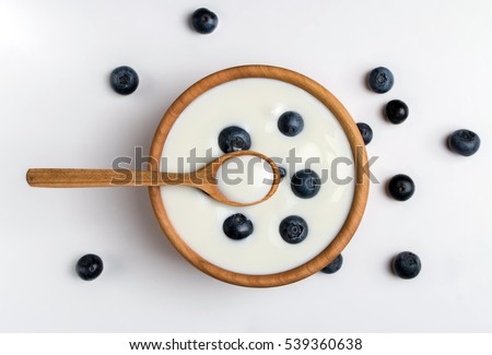 White yogurt in natural wooden bowl with blueberries. Top view.