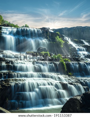 Tropical rain forest landscape with flowing blue water of Pongour waterfall at sunny day under blue sky. Da Lat, Vietnam