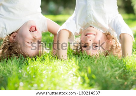 Happy children standing upside down on green grass in spring park. Healthy lifestyles concept.