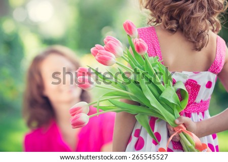 Woman and child with bouquet of flowers against green blurred background. Spring family holiday concept. Women's day