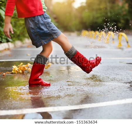 Child wearing red rain boots jumping into a puddle. Close up