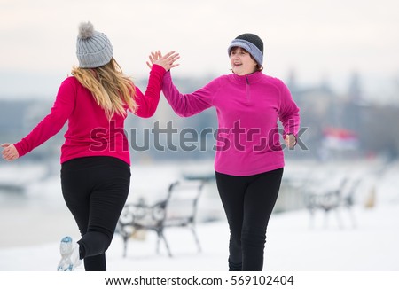 Mother and daughter wearing sportswear and running on snow during winter
