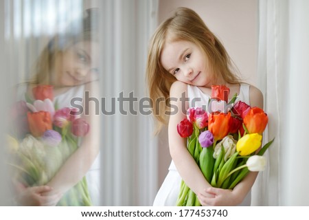 Adorable smiling little girl with tulips by the window - stock photo