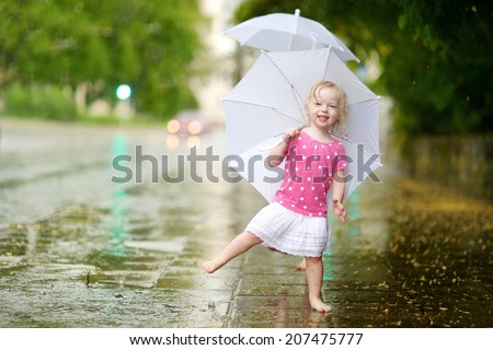 Cute little toddler girl standing in a puddle holding umbrella on a rainy summer day