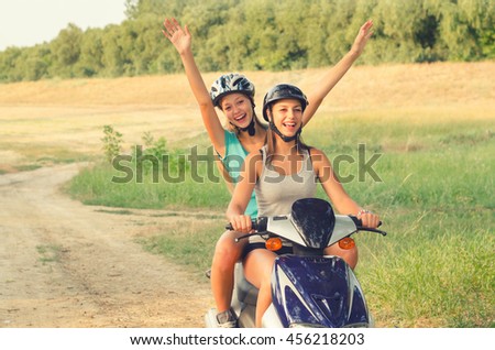 Two Smiling Happy Teenage Girls Riding Scooter Motorcycle On Sunny Summer Day Two Smiling Happy Teenage Girls Riding Scooter Motorcycle On Sunny Summer Day