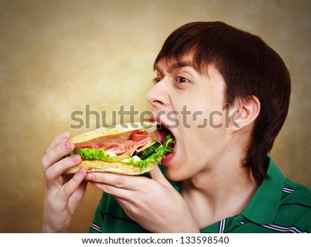 The hungry young man aggressively eats a hamburger. Fast food - stock photo