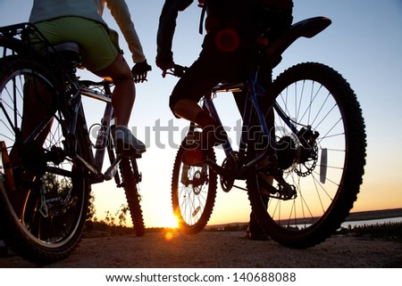 Couple of bicyclists on the brink of rock looks at sunset