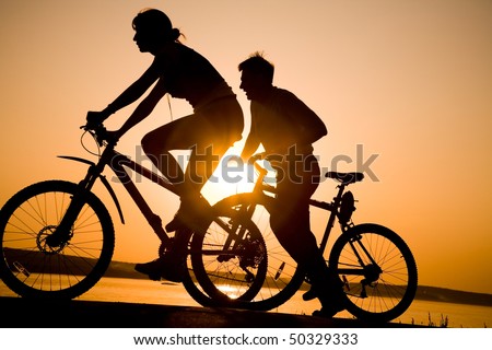 Image of sporty couple on bicycles outdoors against sunset. Silhouette.