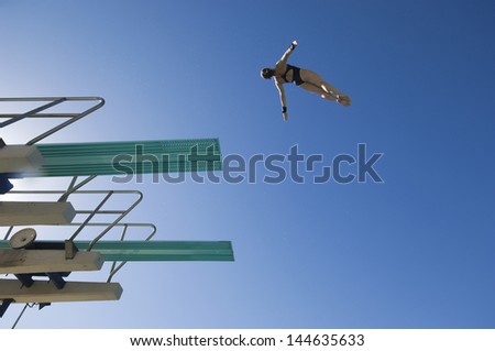 Low Angle View Of A Female Swimmer Preparing To Dive From Diving Board Against Clear Blue Low Angle View Of A Female Swimmer Preparing To Dive From Diving Board Against Clear Blue