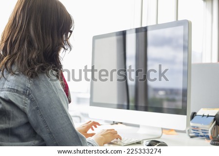 Rear view of businesswoman using desktop computer in creative office