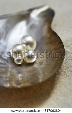 Four pearls in open oyster shell on beach close up elevated view