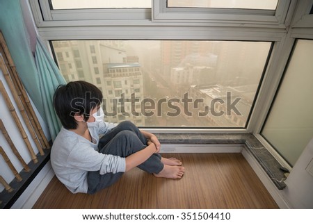 Mask-wearing boy looking outside the window on extremely polluted day