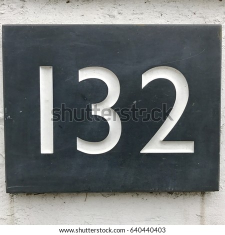 Number 132 one hundred and thirty two carved stone house number address sign on painted white stone wall textured background