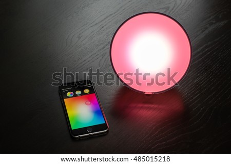 Ostfildern, Germany - September 4, 2016: The Philips Hue app on an Apple iPhone is used to control a Philips Hue smart home light on a dark wooden table or shelf. Using the Apple HomeKit technology