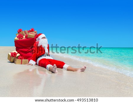 Christmas Santa Claus with sack full of golden gift boxes with red bows resting at ocean tropical sandy beach - travel destinations for vacation to hot countries concept
