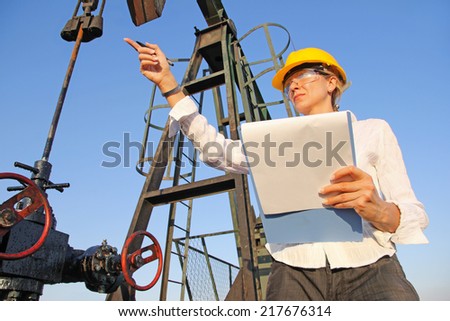 Female engineer writing on clipboard in oil field. She showing by hand what needs to be fixed