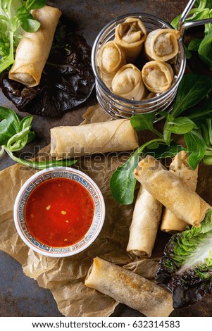Fried spring rolls with red pepper sauce, served on crumpled paper and in fry basket with fresh green salad over old metal texture background. Top view. Asian food