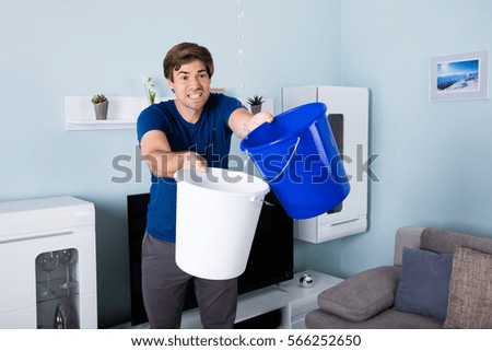Young Male Worried Man Holding Bucket While Water Droplets Leaking From Ceiling Young Male Worried Man Holding Bucket While Water Droplets Leaking From Ceiling