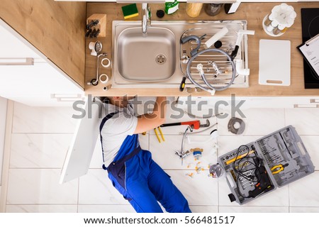 High Angle View Of Male Plumber In Overall Fixing Sink Pipe
