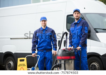 Portrait Of Two Happy Male Janitors Standing With Cleaning Equipment