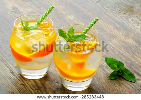 Cold drinks with ice and mint. Orange cocktail on rustic wooden table - stock photo