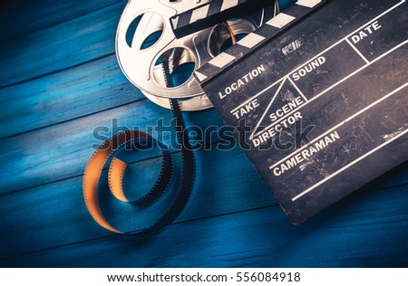 35mm film, reel and movie clapper with dramatic lighting on a wooden background