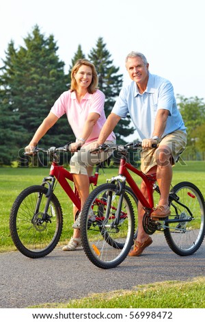 Happy elderly seniors couple biking in park