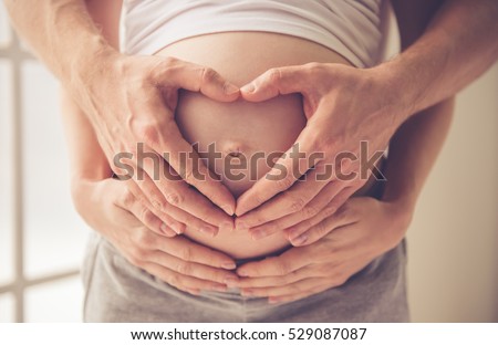 Cropped image of beautiful pregnant woman and her handsome husband hugging the tummy
