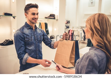 Handsome shop assistant is smiling while giving purchases and credit card to beautiful client