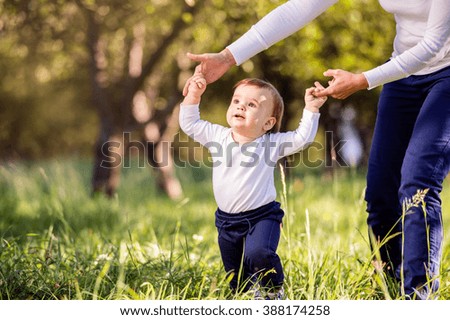 Mother holding hands of her son making first steps