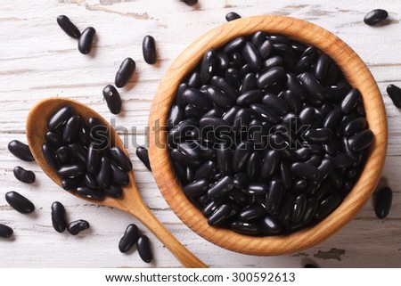 Raw black beans in a wooden spoon and a bowl close up on the table. horizontal view from above