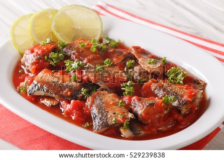 Braised sardines in tomato sauce with lime and parsley close-up on a plate. horizontal