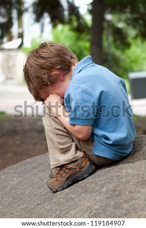 Small child sits on stone in park