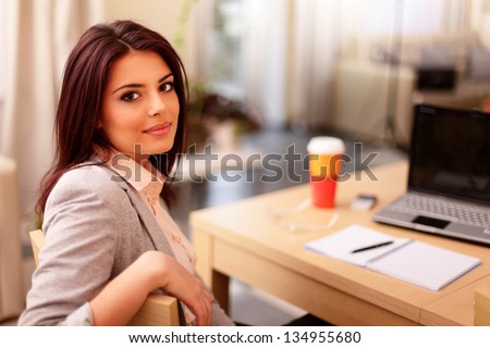 Young businesswoman sitting at desk and working. Smiling and looking back at camera