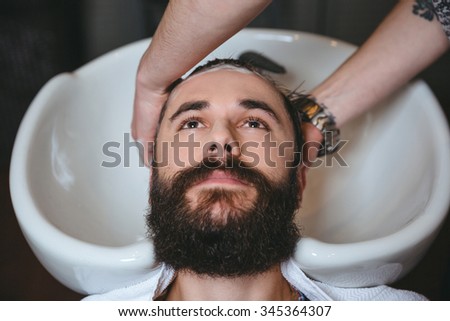 Hairstylist washing head of young attractive man with beard in barbershop