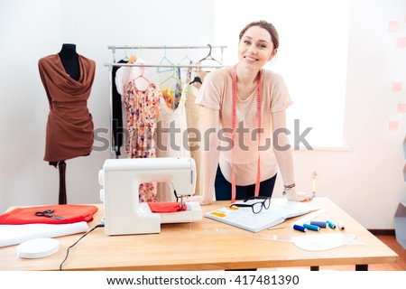 Smiling attractive young woman fashion designer standing and working in studio