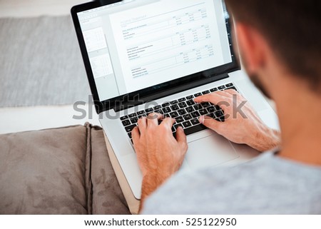 Cropped image of a young man typing on his laptop while sitting on sofa. Focus on hands typing.