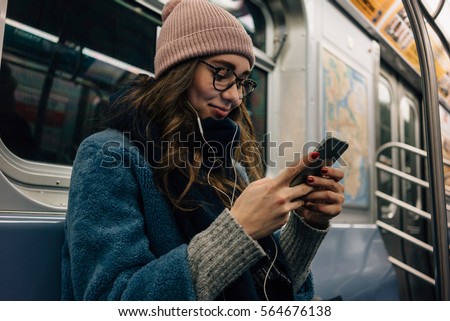 Portrait of a smiling lovely girl typing message on mobile phone in subway train
