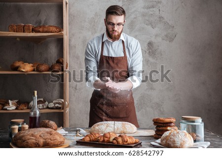 Image of young concentrated bearded man wearing glasses baker cut the bread.