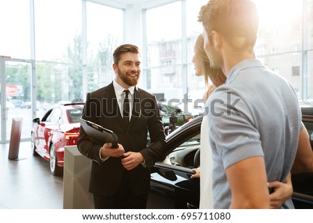 Smiling salesman showing new car to a couple in showroom salon