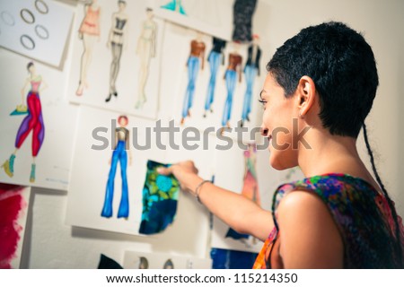 Young people and small business, hispanic woman at work as fashion designer and tailor, looking at sketches of new collection in atelier