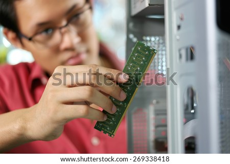 Young asian shop owner working in computer store, repairing computer and adding ram to pc. Focus on hand holding bank of RAM