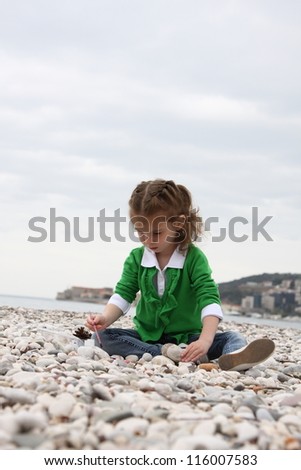 Girl draws on the sea on the stones and pebbles