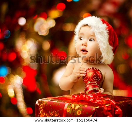 Christmas baby in santa hat holding red ball near present gift box - stock photo