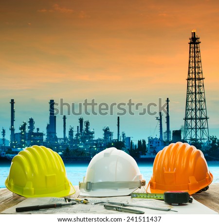 safety helmet on engineer working table against beautiful oil refinery in industry estate