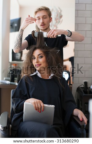 Shot of stylist-barber who does styling comb, brushing a beautiful young model. Beauty Salon- Stylist makes hair beautiful girl with a tablet. a satisfied client in the beauty salon.
