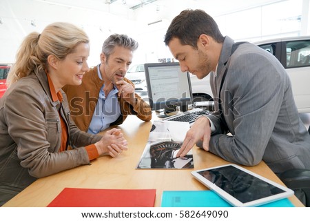 Salesman in car dealership and couple looking at catalogue