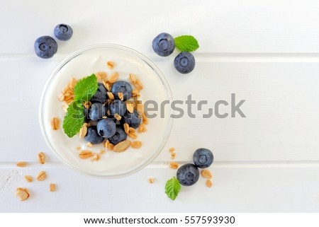 Greek yogurt with blueberries and granola, above view on white wood